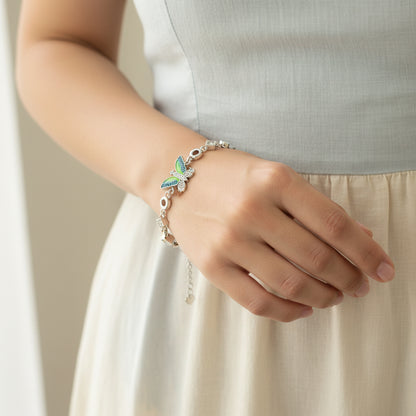 Close-up of a hand wearing a bracelet with a butterfly charm on a neutral background